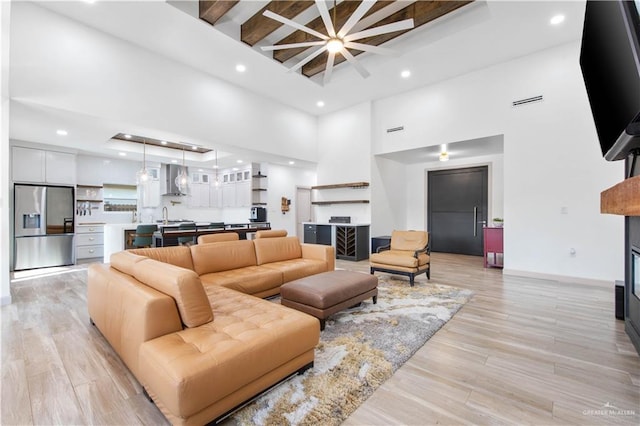 living room with light wood-style floors, a high ceiling, baseboards, beam ceiling, and recessed lighting