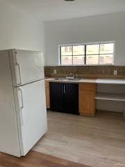 kitchen with light wood-style floors, brown cabinetry, a sink, and freestanding refrigerator