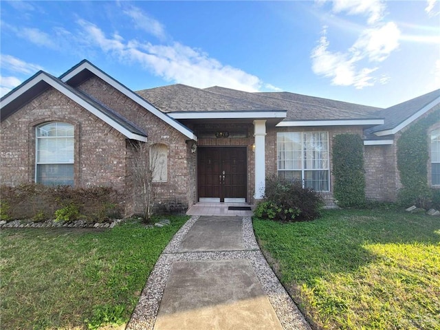 ranch-style home with brick siding, a front lawn, and roof with shingles