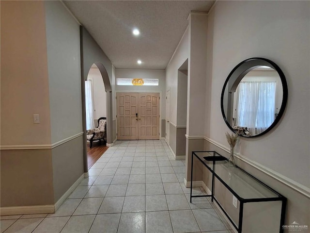 entrance foyer featuring baseboards, recessed lighting, arched walkways, light tile patterned flooring, and a textured ceiling