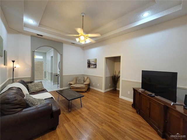 living room with visible vents, light wood-type flooring, arched walkways, a raised ceiling, and a ceiling fan