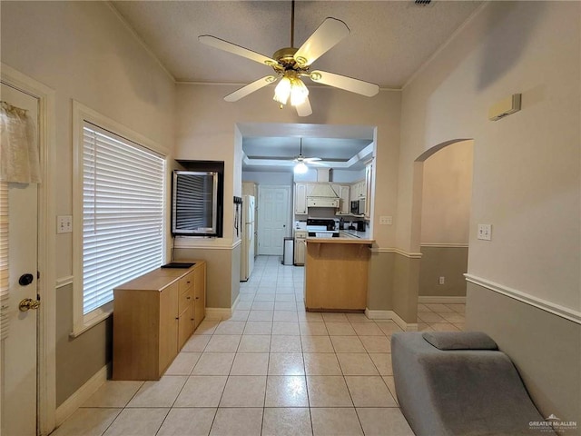 kitchen with electric stove, freestanding refrigerator, a peninsula, light tile patterned flooring, and ceiling fan