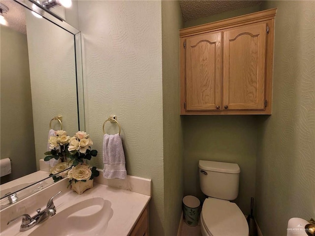 half bathroom with toilet, vanity, and a textured wall