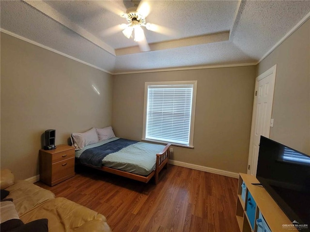 bedroom with a textured ceiling, a raised ceiling, baseboards, and wood finished floors