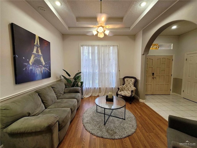 living area featuring a raised ceiling, a ceiling fan, wood finished floors, arched walkways, and baseboards