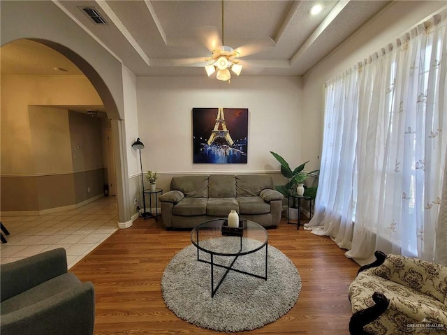 living area with arched walkways, a raised ceiling, a ceiling fan, and wood finished floors