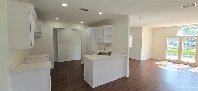 kitchen with a sink, dark wood-style flooring, visible vents, wall chimney range hood, and open shelves
