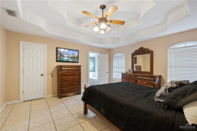 tiled bedroom with ceiling fan, a raised ceiling, and ensuite bath