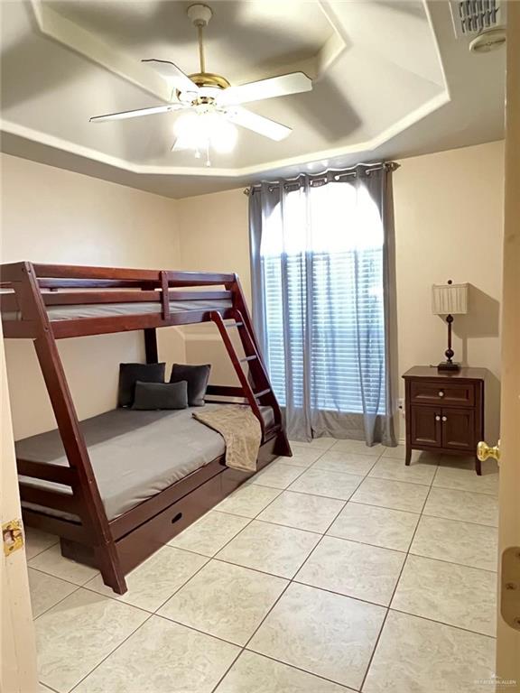 tiled bedroom featuring a raised ceiling and ceiling fan