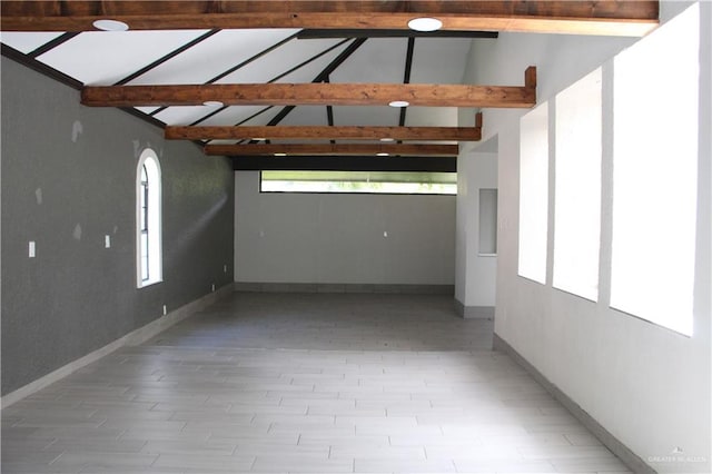 empty room with vaulted ceiling with beams and a wealth of natural light