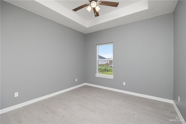 spare room with ceiling fan, light wood-type flooring, and a tray ceiling