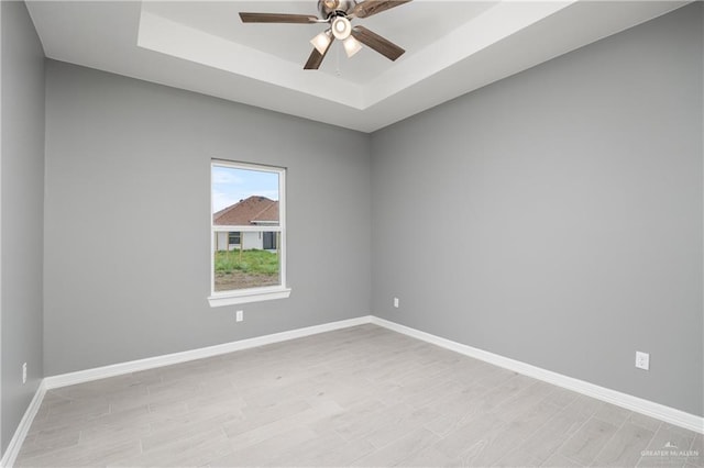 spare room with light wood-type flooring, a tray ceiling, and ceiling fan