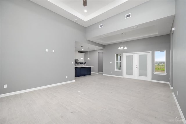 unfurnished living room with a high ceiling, french doors, a raised ceiling, light hardwood / wood-style flooring, and a chandelier