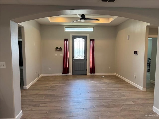 entryway with a raised ceiling, ceiling fan, and light hardwood / wood-style floors