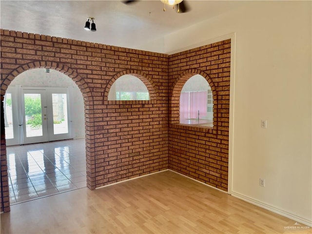 spare room featuring ceiling fan, french doors, brick wall, and light wood-type flooring