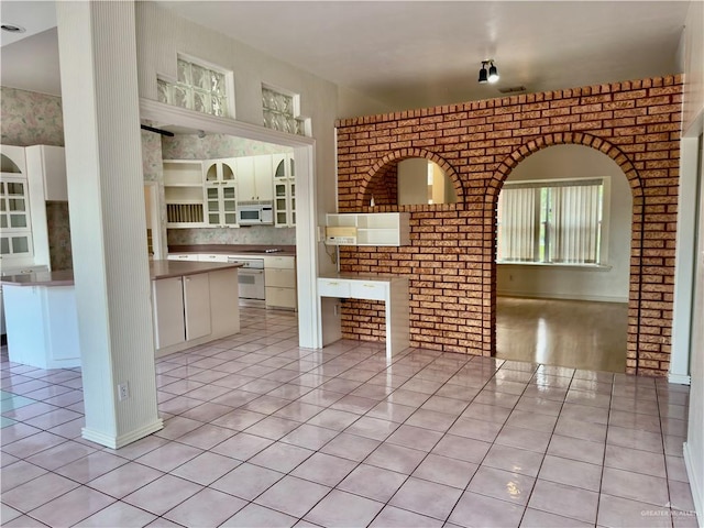 kitchen with light tile patterned floors, white appliances, and brick wall