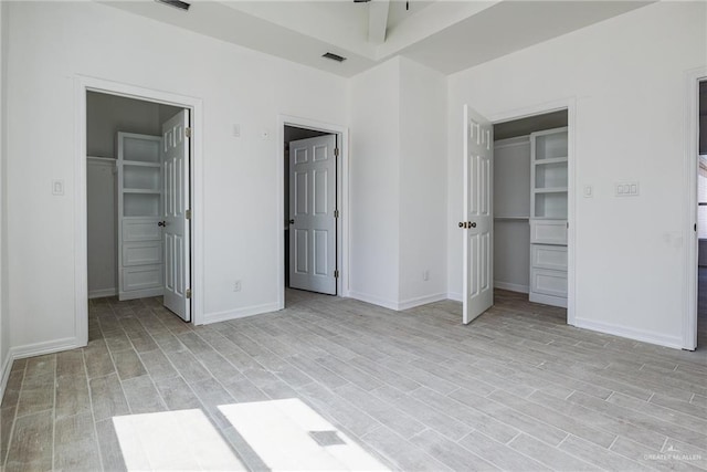 unfurnished bedroom featuring light wood-type flooring, visible vents, a closet, and a walk in closet