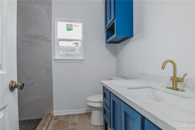 full bathroom featuring toilet, a tile shower, baseboards, wood finished floors, and vanity