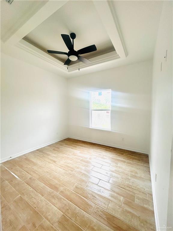 empty room with a raised ceiling, light wood finished floors, baseboards, and a ceiling fan