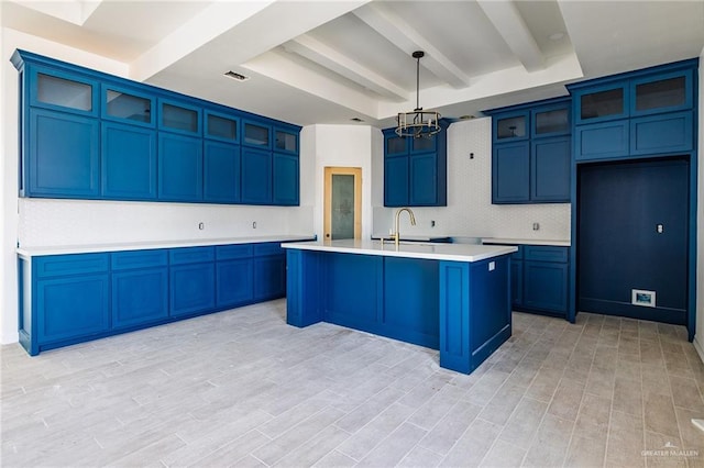 kitchen featuring blue cabinetry, a notable chandelier, a kitchen island with sink, and beamed ceiling