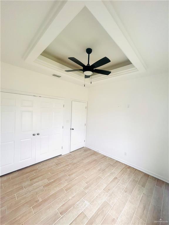 unfurnished bedroom featuring visible vents, a closet, light wood-style floors, and a raised ceiling