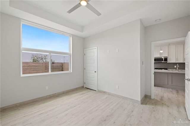 1216 N Lincoln Ave, San Juan, TX 78589 - unfurnished room with a ceiling fan, light wood-style flooring, a sink, a raised ceiling, and baseboards
