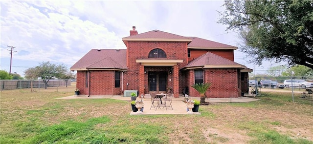 rear view of house with a patio, a chimney, fence, a yard, and brick siding