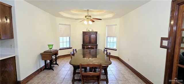 dining area with a ceiling fan, a tray ceiling, a healthy amount of sunlight, and baseboards