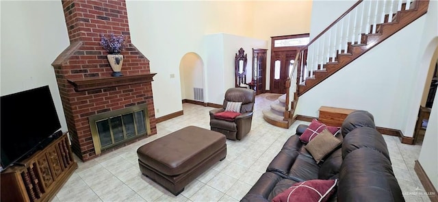 living room featuring arched walkways, visible vents, a brick fireplace, baseboards, and stairs