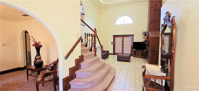 entrance foyer with stairway, a towering ceiling, visible vents, and baseboards