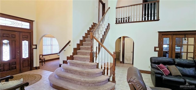 entrance foyer with arched walkways, light tile patterned floors, a towering ceiling, and stairs