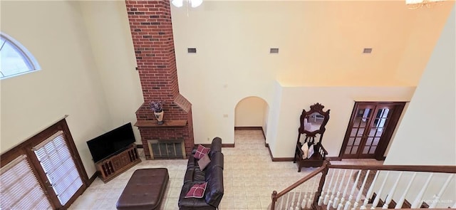 living room with visible vents, baseboards, arched walkways, a towering ceiling, and a brick fireplace