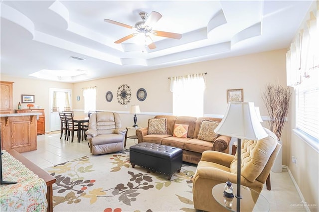 living room featuring light tile patterned flooring, ceiling fan, and a tray ceiling