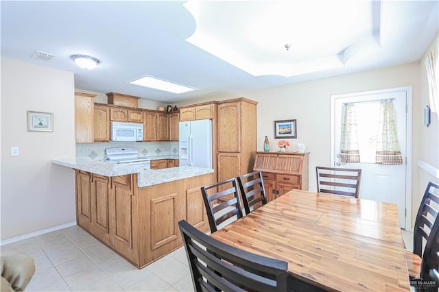 kitchen featuring white appliances, light stone counters, a raised ceiling, light tile patterned flooring, and kitchen peninsula