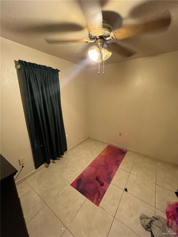 empty room with light tile patterned floors, a textured ceiling, baseboards, and a ceiling fan