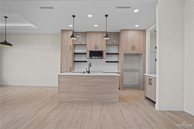 kitchen with a center island, decorative light fixtures, light brown cabinetry, sink, and light wood-type flooring