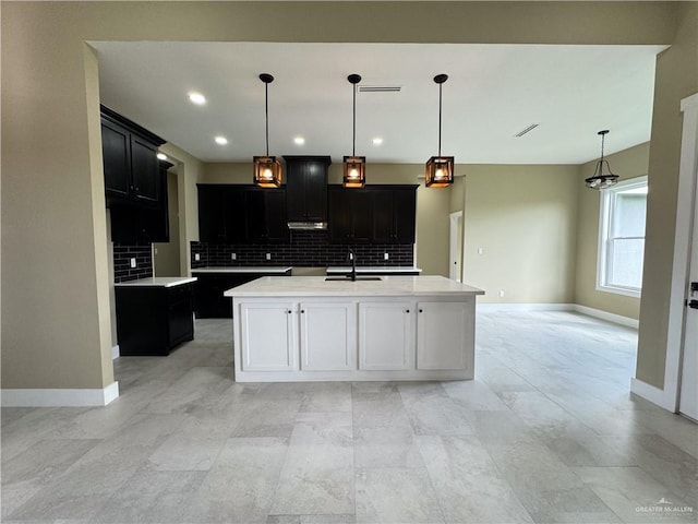 kitchen with decorative backsplash, sink, a kitchen island with sink, and hanging light fixtures