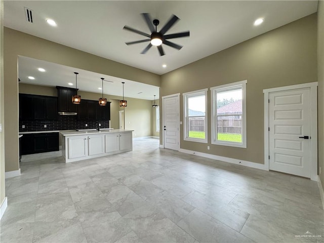 kitchen featuring decorative backsplash, ceiling fan, an island with sink, and hanging light fixtures