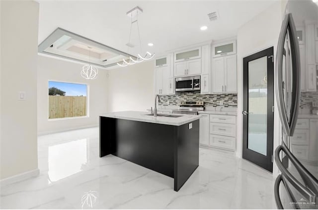 kitchen with a kitchen island with sink, white cabinets, sink, appliances with stainless steel finishes, and decorative light fixtures