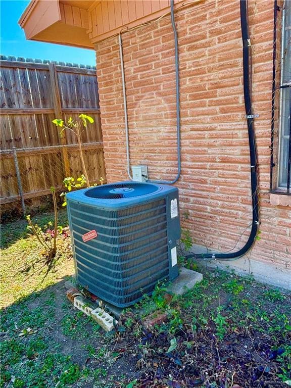 details featuring cooling unit, brick siding, and fence