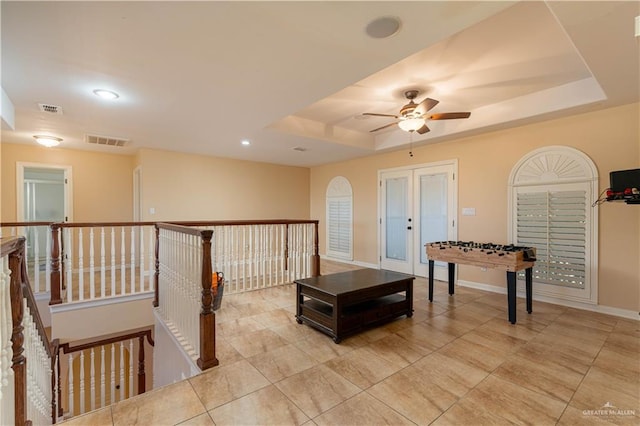 playroom featuring ceiling fan, french doors, and a tray ceiling