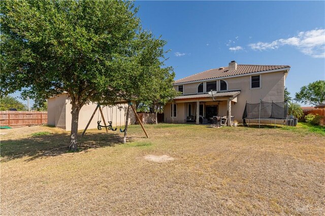 back of house featuring a trampoline and a lawn