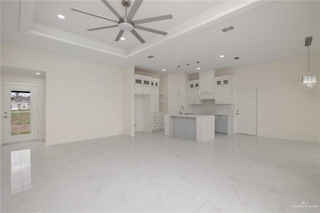 unfurnished living room featuring a raised ceiling, sink, and ceiling fan with notable chandelier