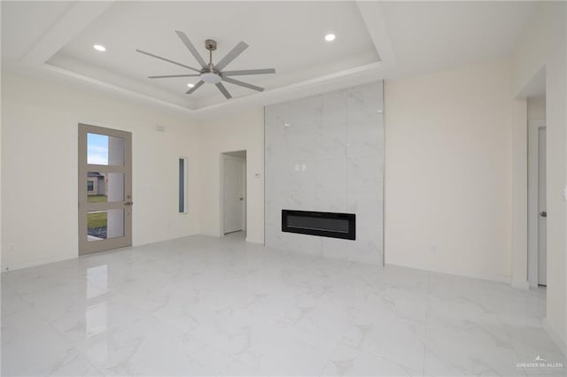 unfurnished living room with a raised ceiling, ceiling fan, and a fireplace