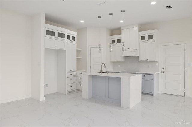 kitchen with pendant lighting, white cabinetry, sink, and a center island with sink