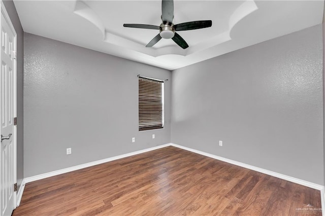 empty room featuring hardwood / wood-style flooring, a tray ceiling, and ceiling fan