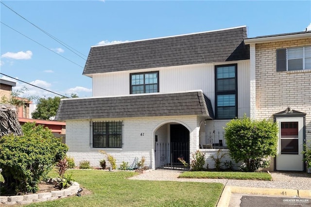 view of front of home with mansard roof, a shingled roof, brick siding, and a front yard