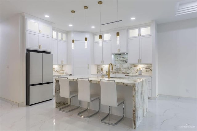 kitchen with sink, white cabinetry, light stone counters, a center island with sink, and stainless steel refrigerator