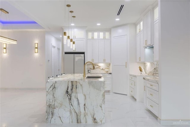 kitchen featuring sink, refrigerator, white cabinetry, hanging light fixtures, and an island with sink