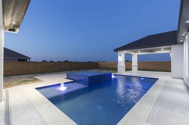 pool at dusk featuring pool water feature, a patio area, and a jacuzzi